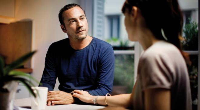 Un couple discute autour d'une table, la femme tient le poignet de l'homme.